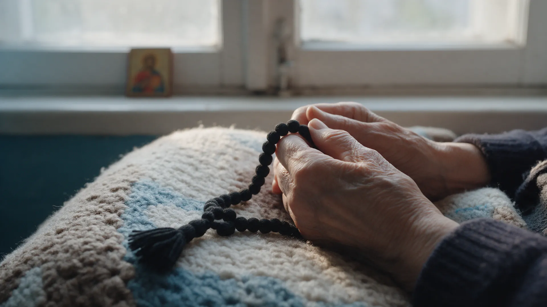 Hands holding a prayer rope by a window